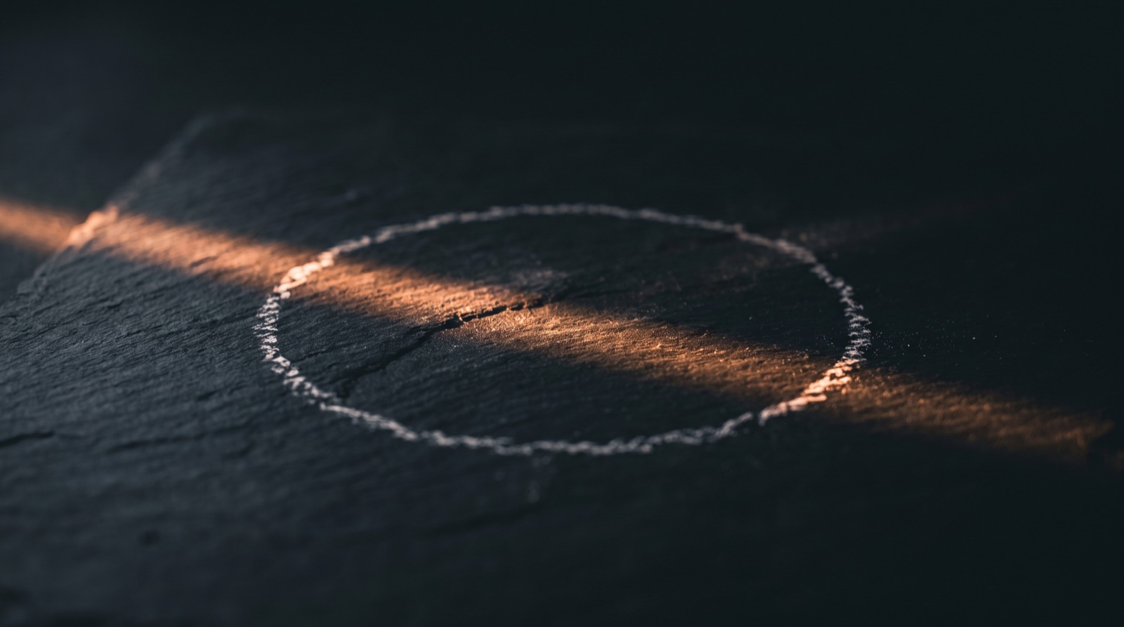 A circle drawn on dark stone with a single thin line of light leading out of it