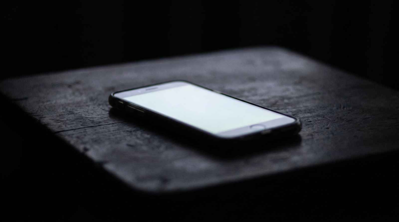 The cold light of a phone on the empty table of a dark room